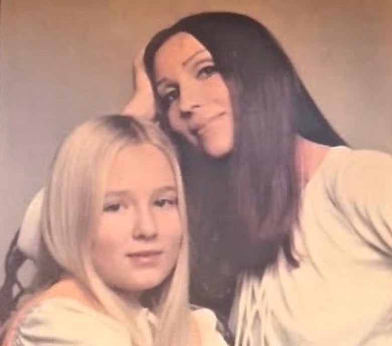 Portrait photograph showing a young girl with long blonde hair photographed next to her mother, who has long dark hair.