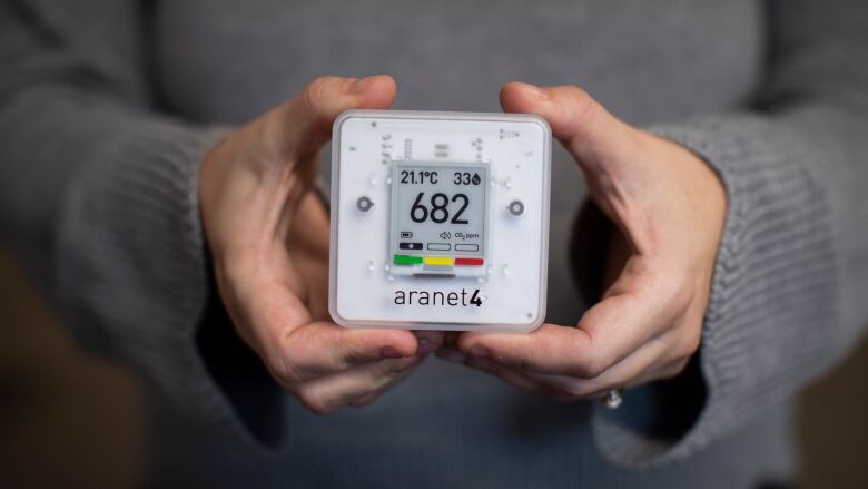 A person holds up a portable device with the reading '682', signifying carbon dioxide concentration in parts per million.