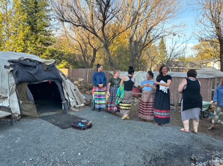 Women in long skirts line up outside a sweat lodge.