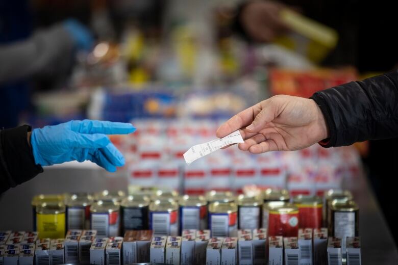 Two hands exchange a bill over stacked cans at a food bank.