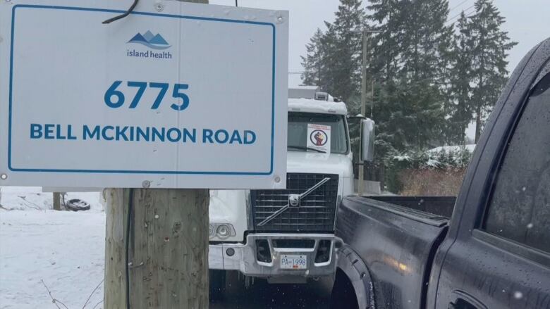 Two trucks stand next to a fence post with the words 'Island Health' and 'Bell McKinnon Road'.