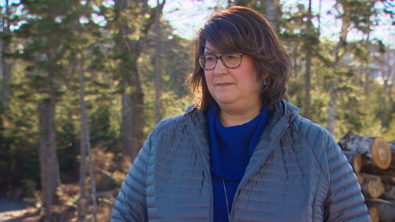 A woman in a blue coat stands near some trees