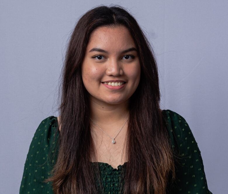 A young woman in a green dress poses and smiles at the camera.