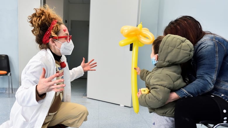 A clown entertains a child holding an animal balloon after receiving a flu vaccine.