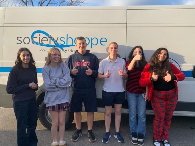 Six students stand in front of a Saint Vincent de Paul bus with their thumbs up.