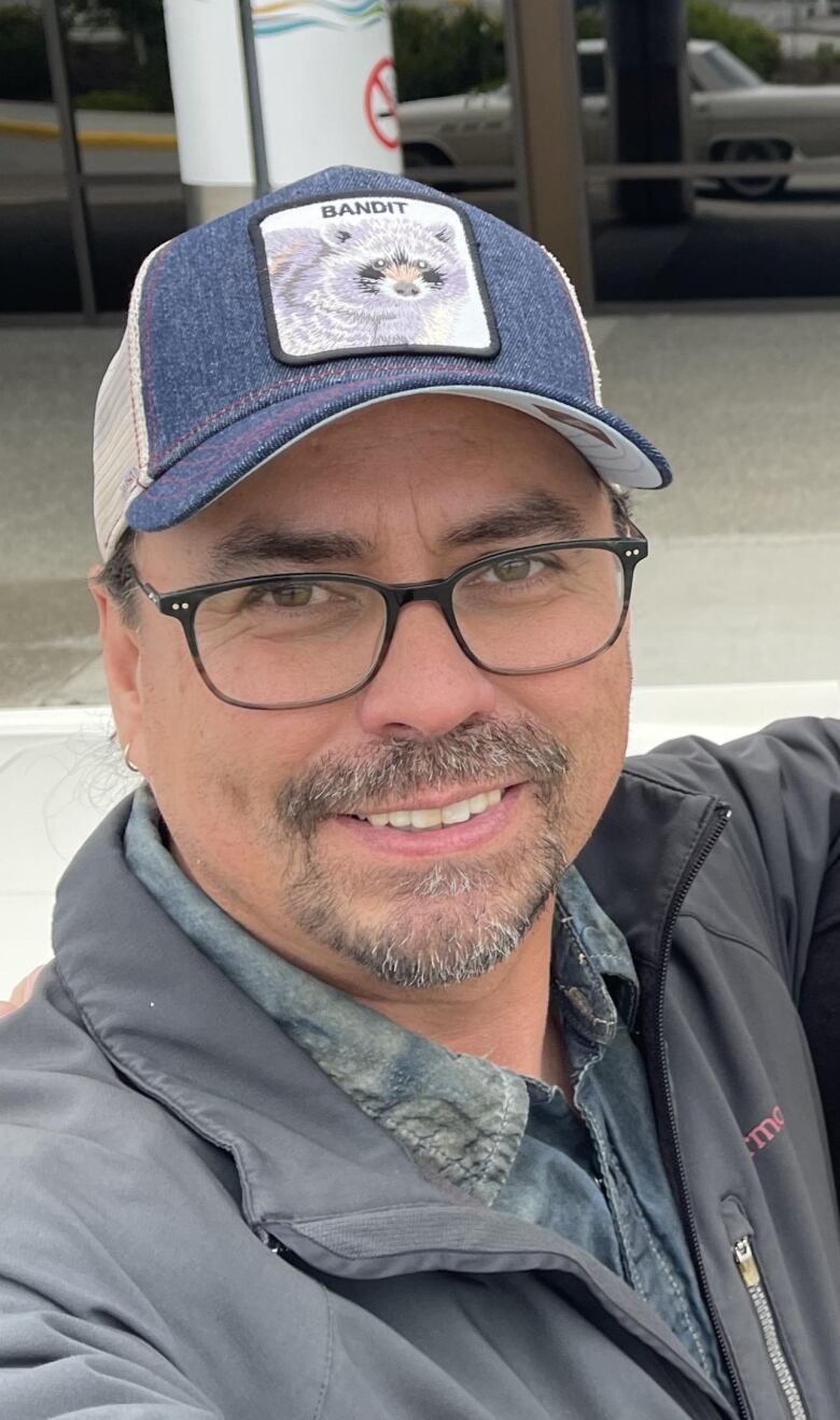 a picture of a smiling man wearing glasses and a baseball cap.