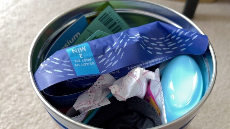 An overhead shot of a tin packed with tampons, deodorant, socks and bus tickets.