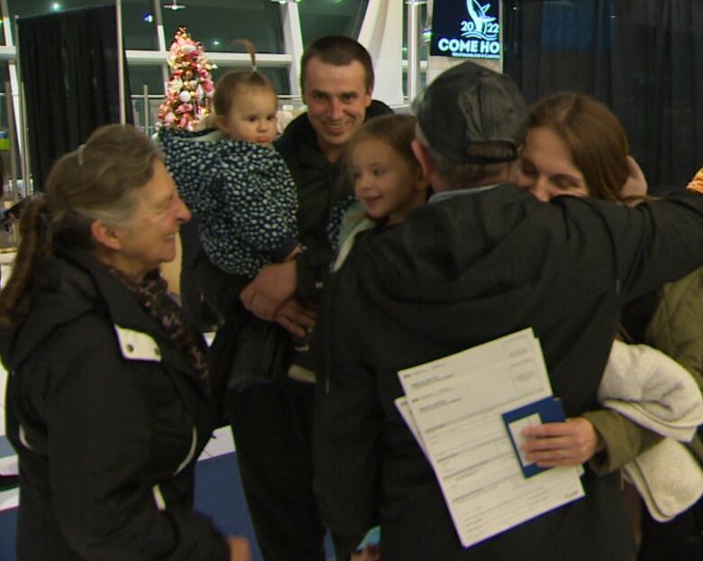 Three people hug while three others look on, smiling.