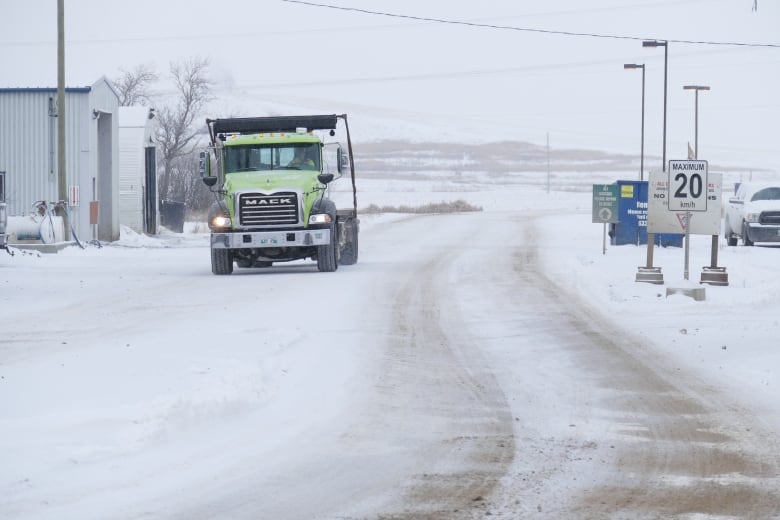 A garbage truck drives down a snowy road.