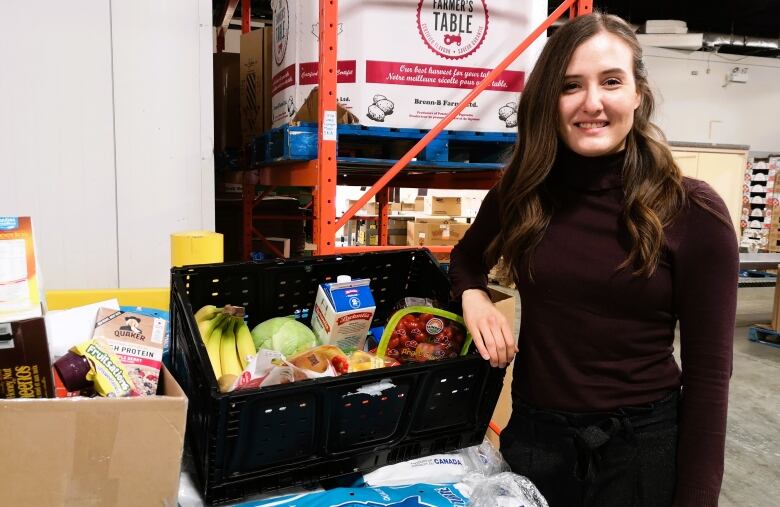 Woman poses beside large box of food in food bank's warehouse