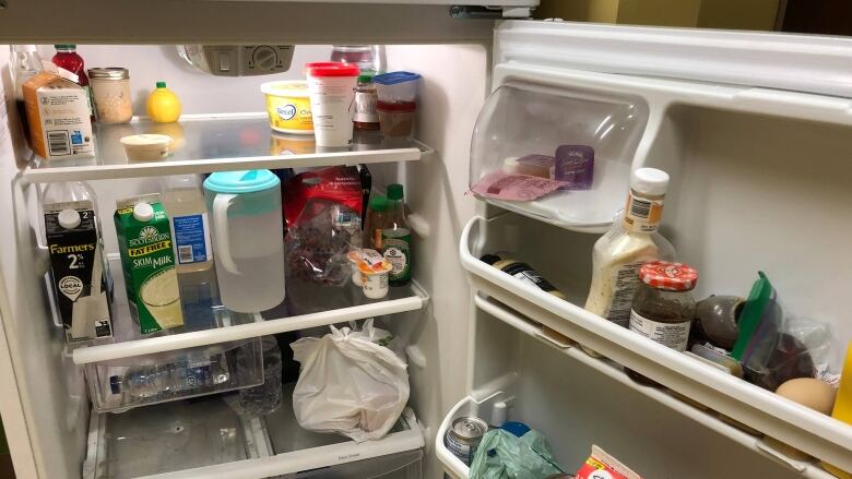 A fridge with its door hanging open, showing various food products inside.