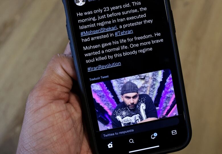 A person holds a phone displaying text and a photo of a protester.