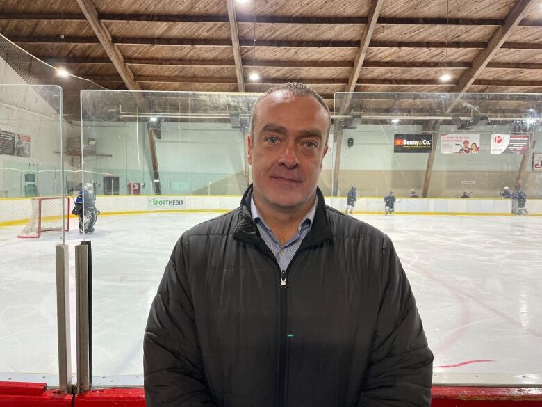 Jason McCaig wearing a black jacket posing in front of the skating rink.