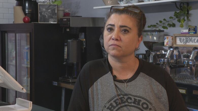 A woman stands at the counter of her sandwich shop, frowning.