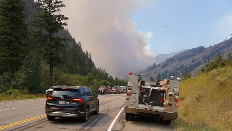 Plumes of smoke rise from the end of a highway filled with firefighting vehicles.