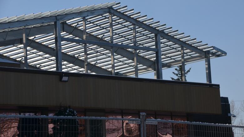 The skeleton a metal roof rises up behind the Sudbury Jail, with construction fencing and equipment in the front yard. 