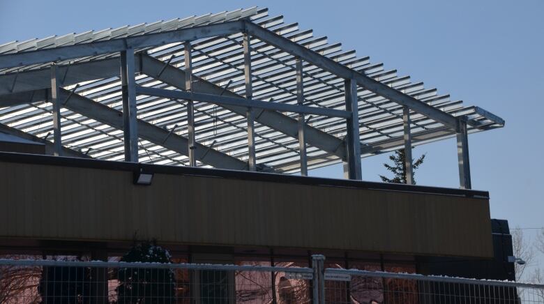 The skeleton a metal roof rises up behind the Sudbury Jail, with construction fencing and equipment in the front yard. 