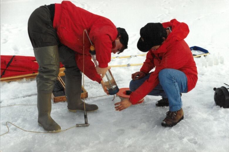 Two people bend over equipment in the snow.