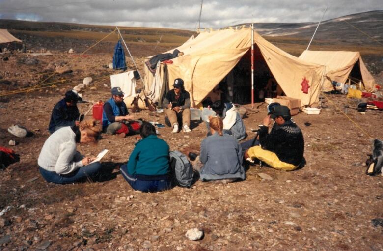 A group of people sit in a circle in front of a tent.