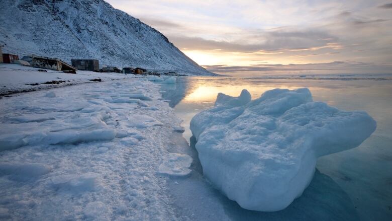 A scenic shot of sunlight glinting off water against a dramatic sky, with ice and snow.