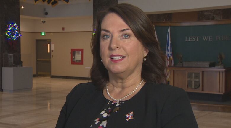 A woman wearing a black jacket and white pearls stands inside Confederation Building.