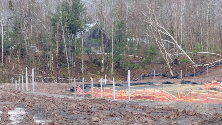 A home is seen behind trees. A muddy construction site with fencing is seen nearby.