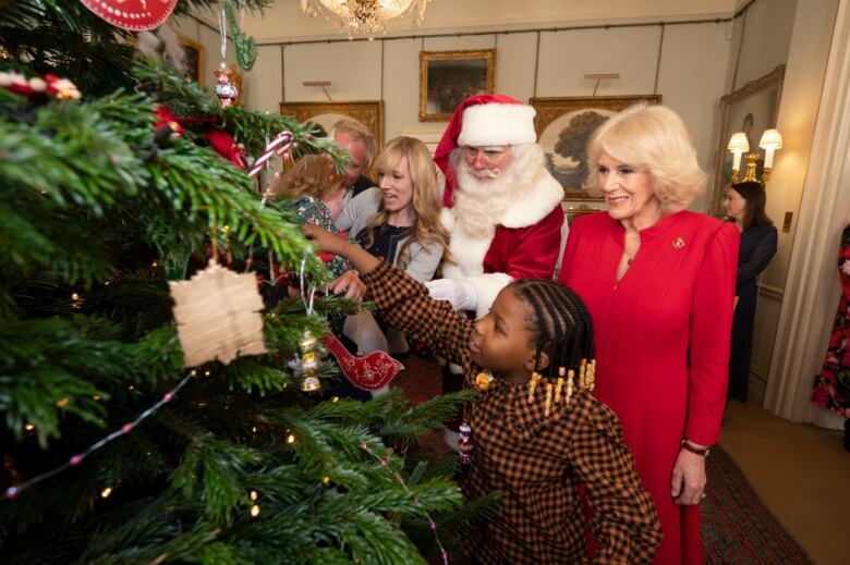 An adult watches as a child helps decorate a Christmas tree.