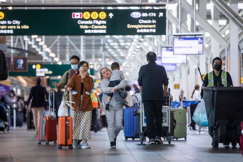 Travellers walk carrying and pushing luggage in an airport.