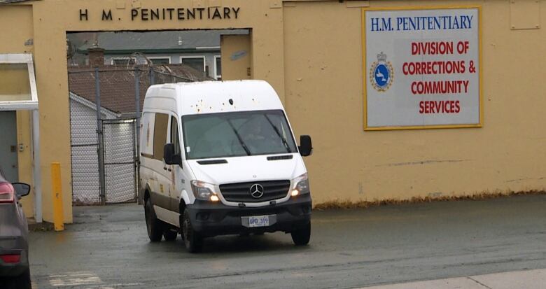 A white van is driving from a yellow stone building. 