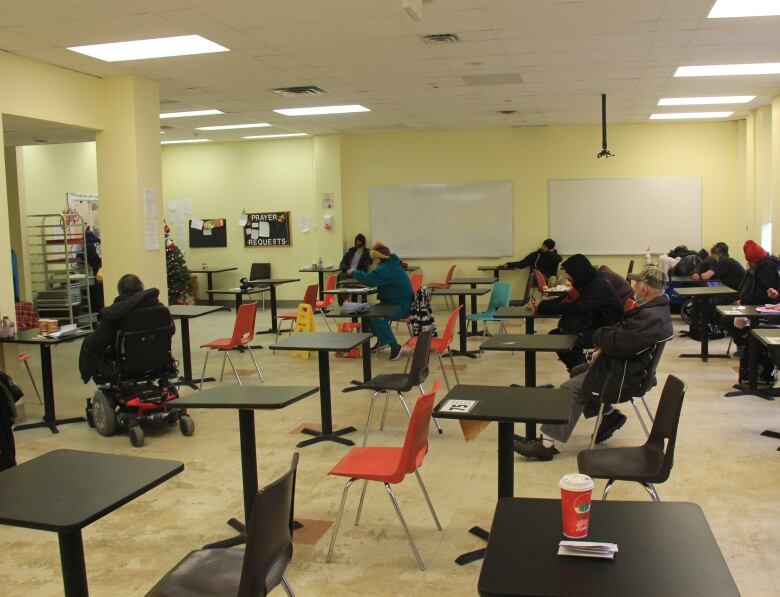 People sit on spread apart chairs at desks.