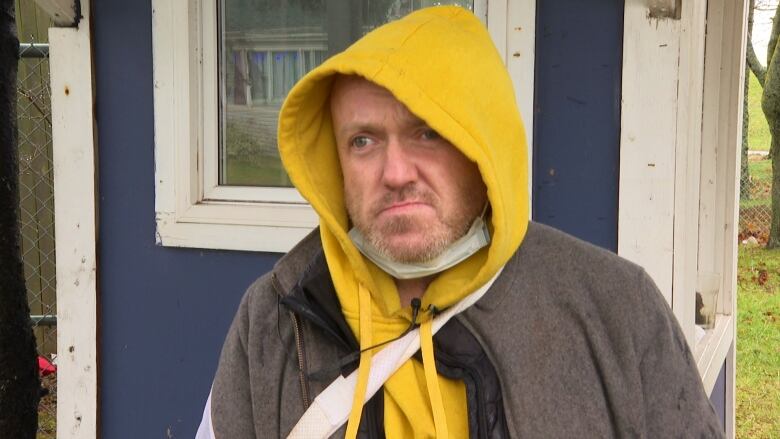 A man in a grey jacket and a yellow hoodie, with a short beard and moustache. 