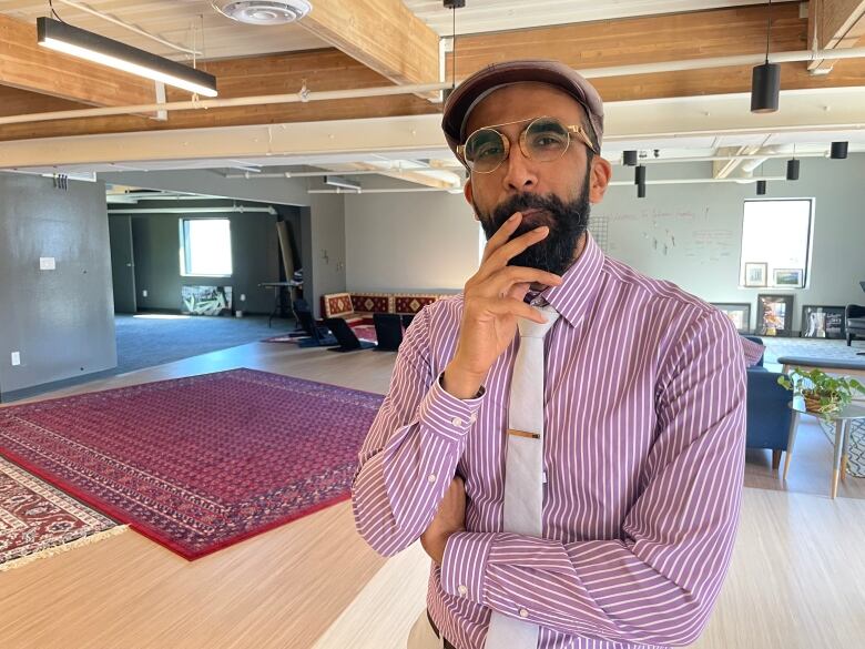 Man in hat and glasses gives thoughtful look to camera.