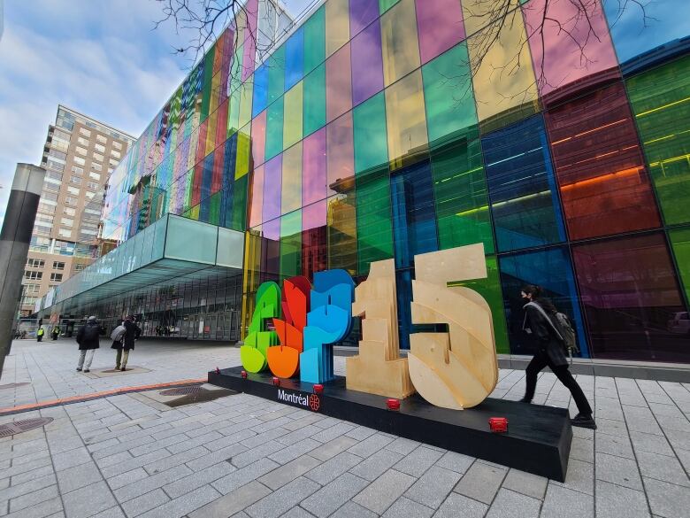 A large sign reads: COP15 in front of Montreal's palais des congres. A person walks past the sign. Trees in the photo are bare. 