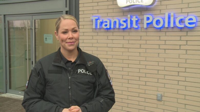 A constable with the Metro Vancouver Transit Police stands in front of her police station, smiling with her hands folded together.