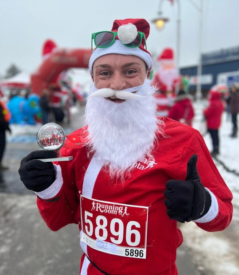 A smiling man in a Santa costume with a trophy for winning the 5k. 