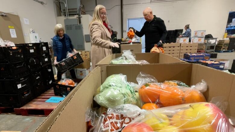 Three volunteers help put vegetables into boxes on a conveyor belt at the Community Kitchen Program of Calgary's warehouse.  