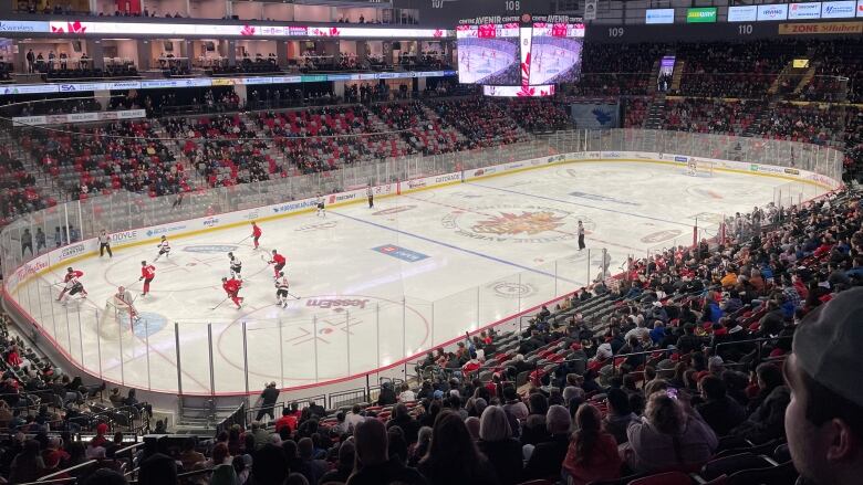 A hockey rink with stands of people surrounding it. Players are concentrated on the left half of the ice.