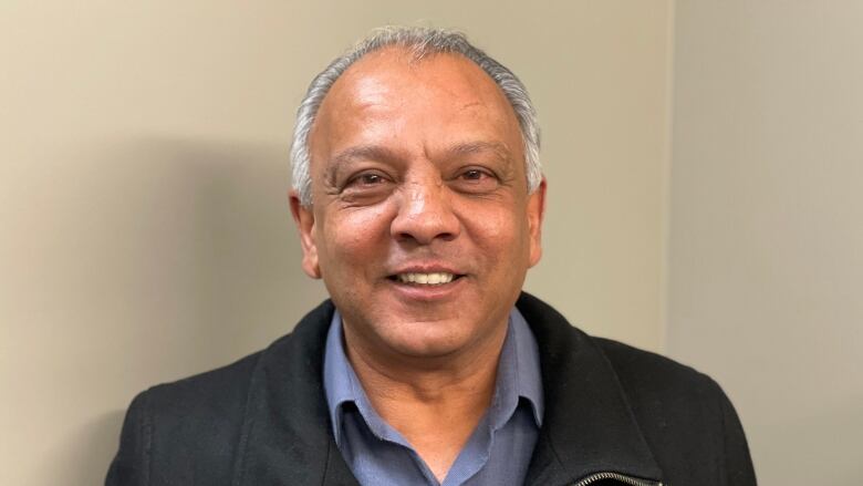 A man smiles in front of a corner of walls.