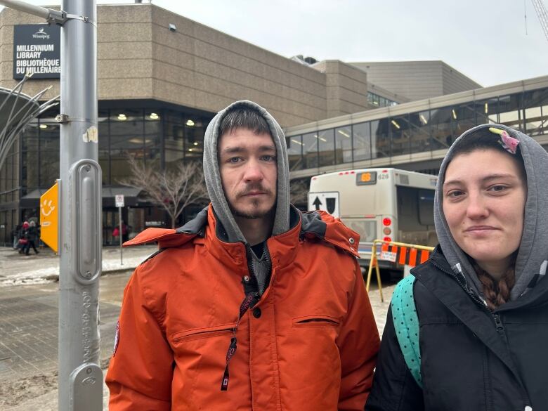 A man and a woman are standing on the street in front of a large building with a sign that says 