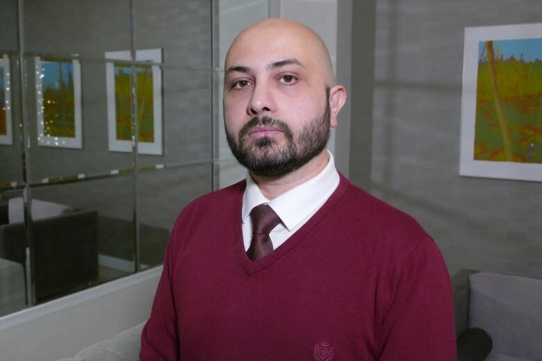 A man in a red sweater, with a short beard and a shaved head, looks at the camera.