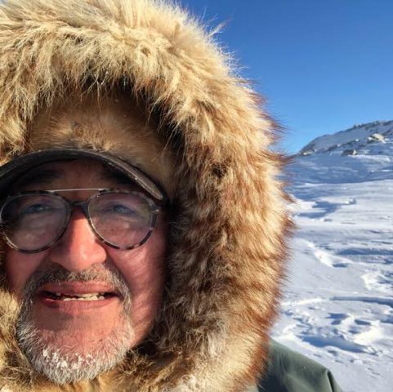 A portrait of a man wearing a parka outdoors in snowy landscape.