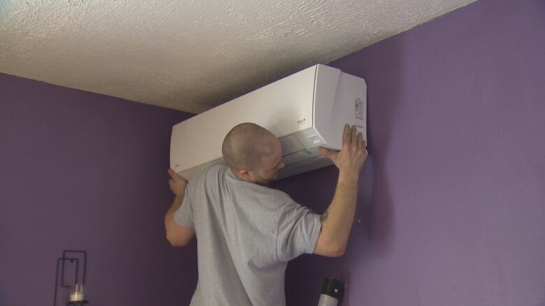 A man installs a heat pump on a purple wall.