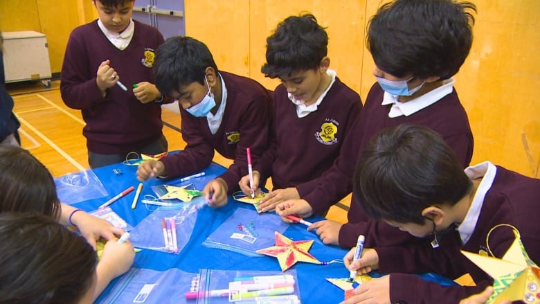 Four students in burgundy school uniforms stand at a table colouring paper stars.