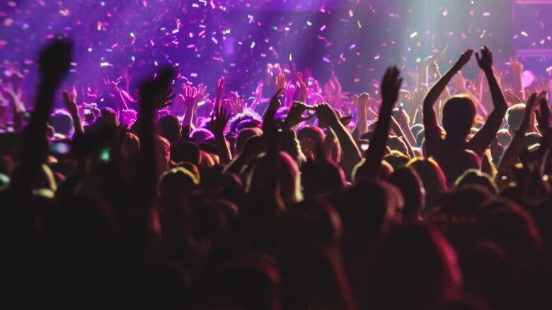 A crowd of people are silhouetted against a bright stage.