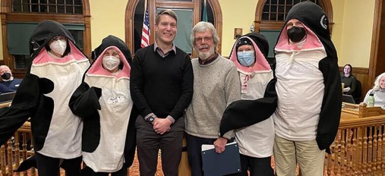 A group of six people, including four in whale costumes, are pictured in what appears to be a U.S. government office.