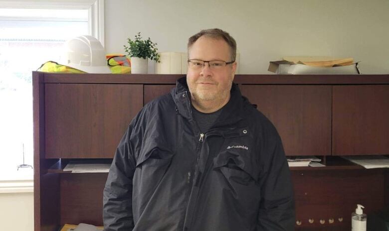 A man wearing a black jacket stands in an office.