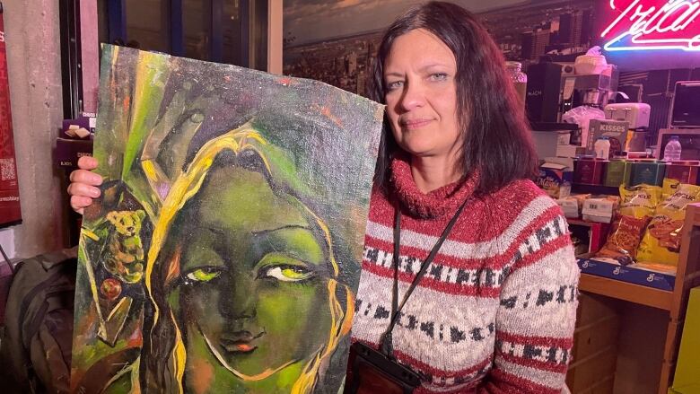 A woman in a sweater poses with her painting.