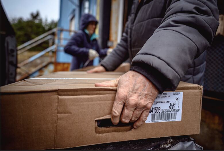 Older man lifting a box of food. This photo shows the man's hand lifting the box.