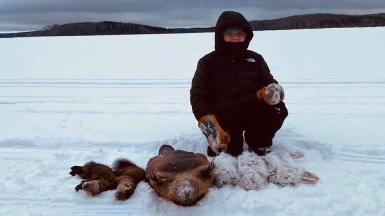 A boy dressed in a warm jacket and mittens poses with rabbits, beaver and marten that he trapped in the winter.