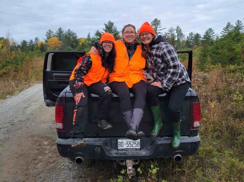 Three women sit on the back of a truck and pose for a photo.